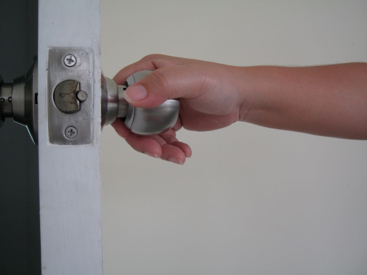 The hand is twisting the knob to open the door. Open the white door with the keys. Door knob with a key.