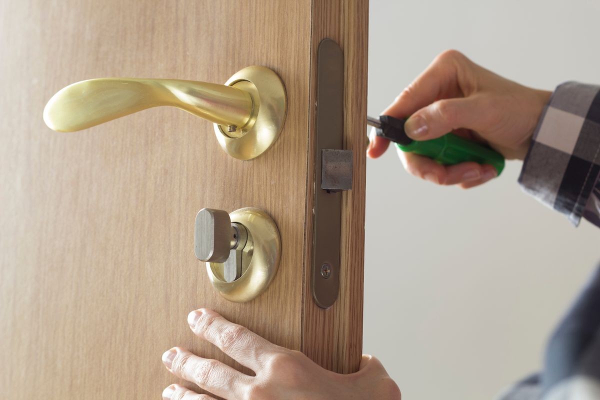 The man repairs the locksmith, sets the door lock on the wooden door.